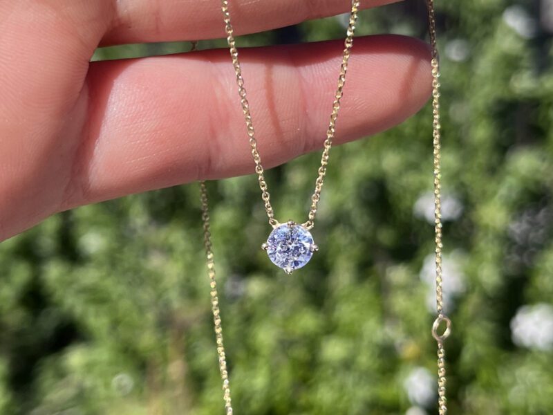 Hand holding necklace with single diamond pendant.