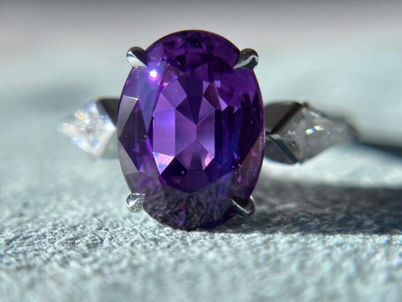Purple gemstone ring on textured surface.