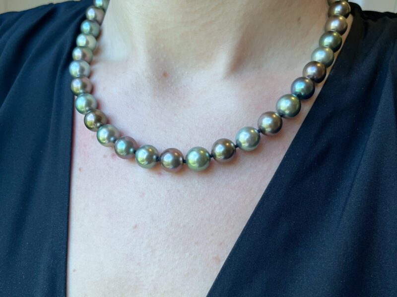 Person wearing a pearl necklace, black top.