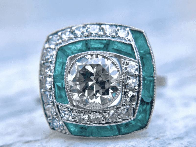A diamond and emerald ring is shown on top of a table.