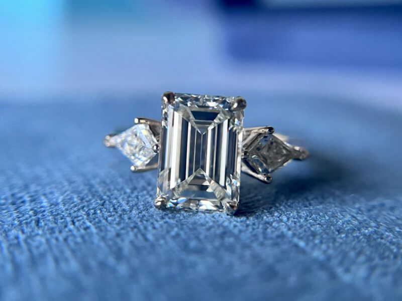 Emerald-cut diamond ring on blue fabric.