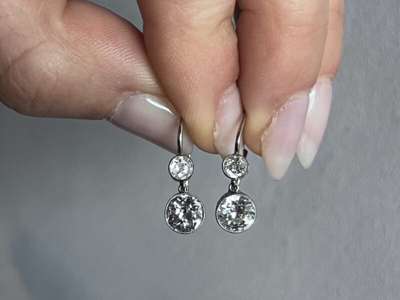 Hand holding two sparkling diamond earrings.