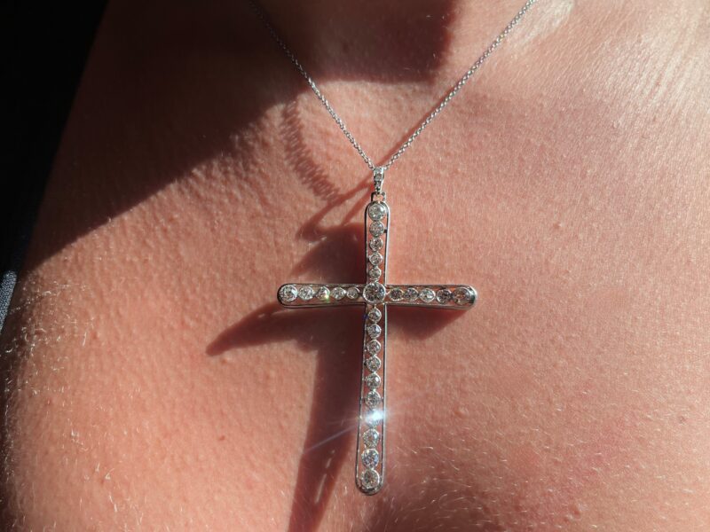 Silver cross necklace in sunlight on skin.